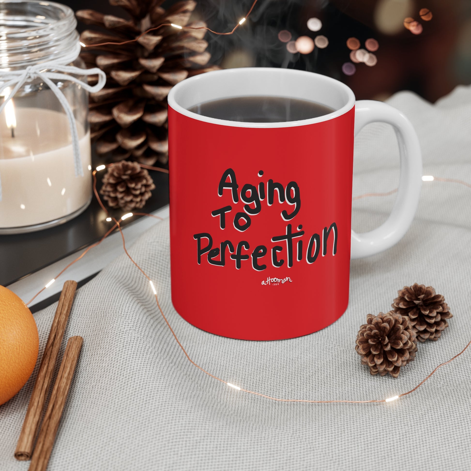 Red mug with 'Aging to Perfection' text on a table with decorative items