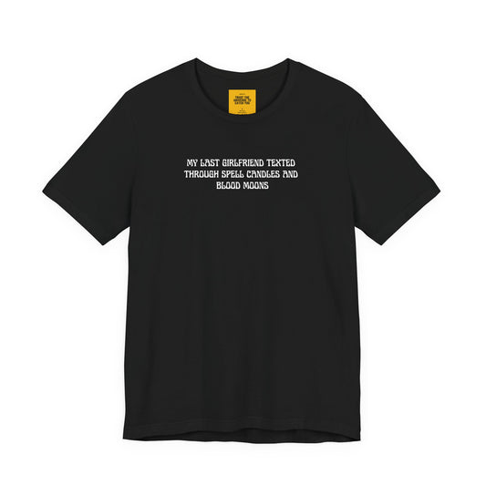 Black t-shirt with white text MY LAST GIRLFRIEND TEXTED THROUGH SPELL CANDLES AND BLOOD MOONS on a white background with Trust the Universe to catch you neck label