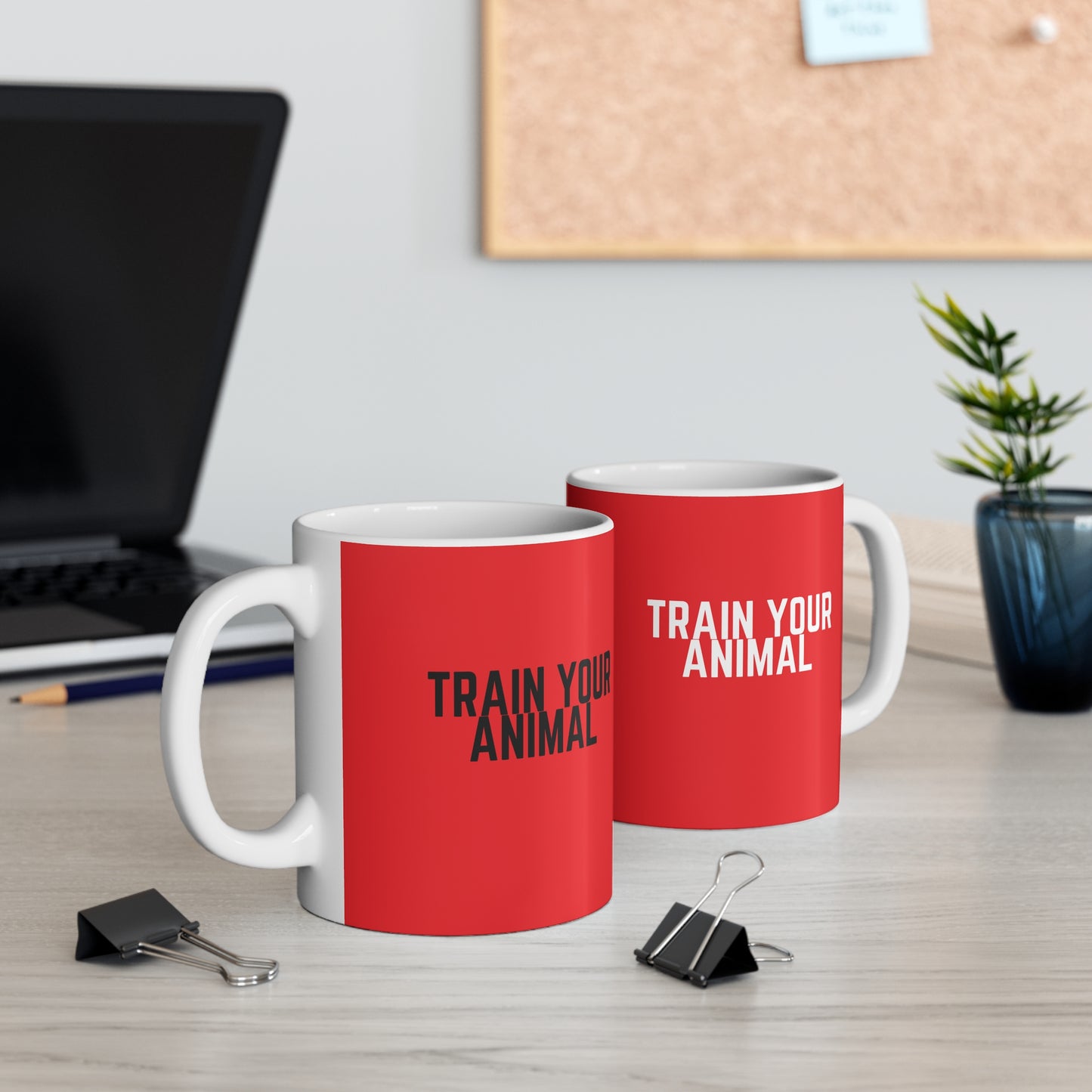 Two red mugs with 'TRAIN YOUR ANIMAL' text on a desk with office items.